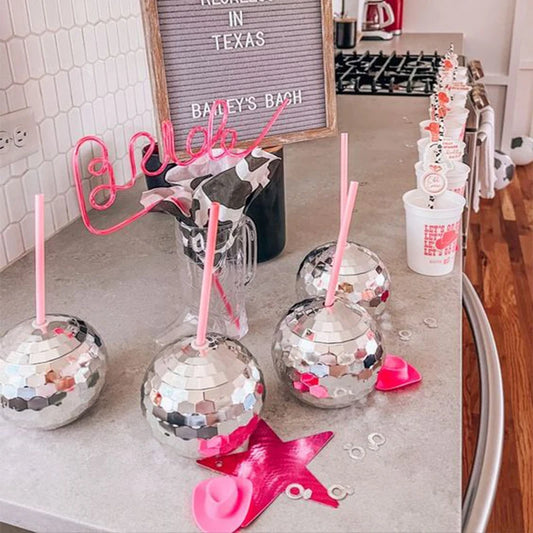 Silver disco balls with pink straws on a kitchen counter, with 'Bailey's Bachelorette' sign in the background.