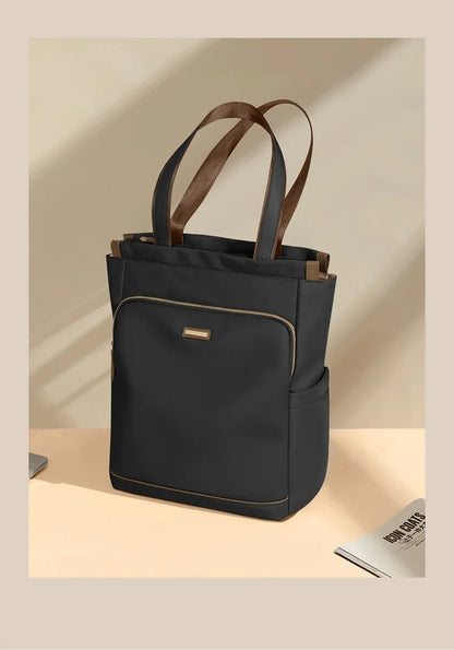 Black tote bag with brown straps on a beige background