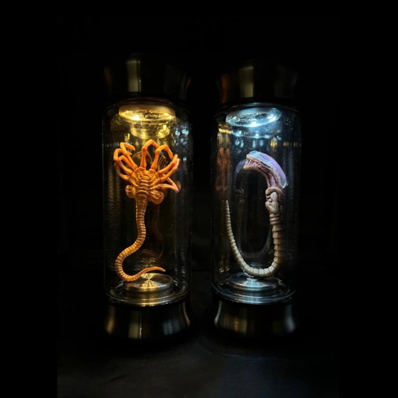 Two alien creature models in glass cases on a dark background
