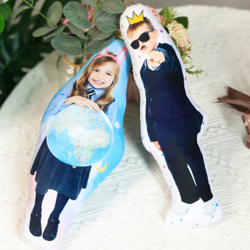Two plush toys with printed images of a girl holding a globe and a boy wearing sunglasses and a crown on a white surface.