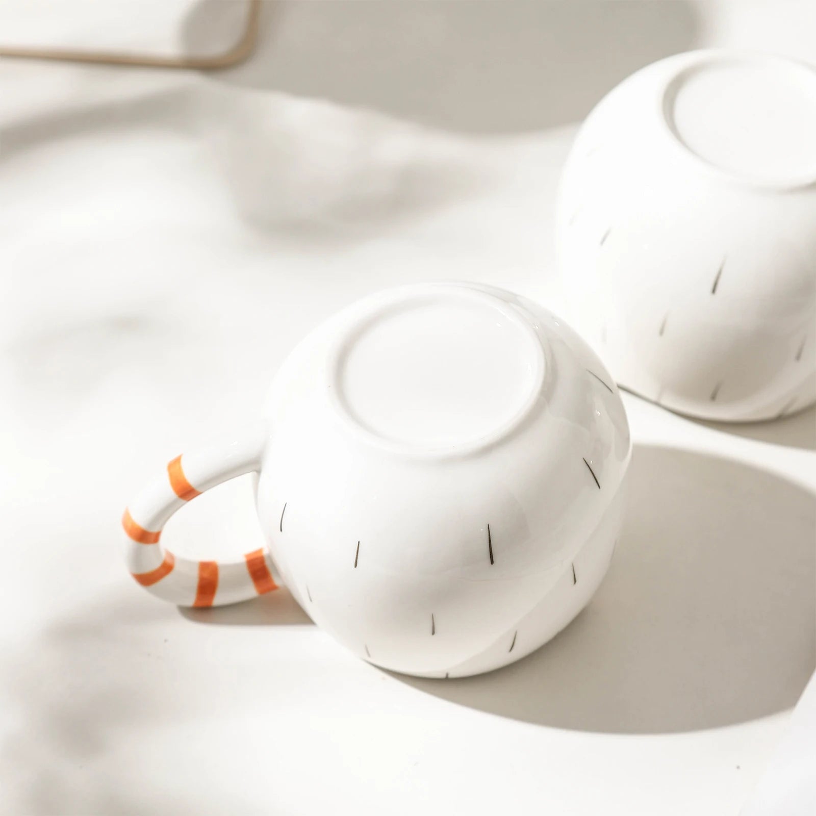 White ceramic teapot and cup with orange handle on a light background