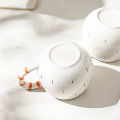 White ceramic teapot and cup with orange handle on a light background