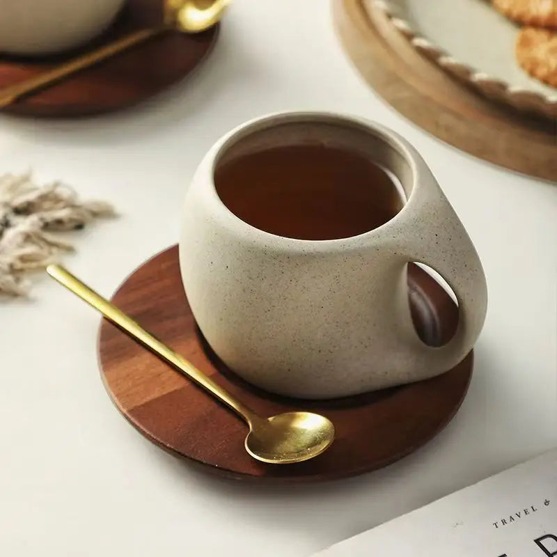 Ceramic cup with a handle on a wooden coaster with a gold spoon, on a light surface.