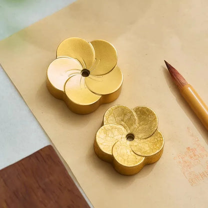 Two gold flower-shaped objects on a textured surface with a pencil.