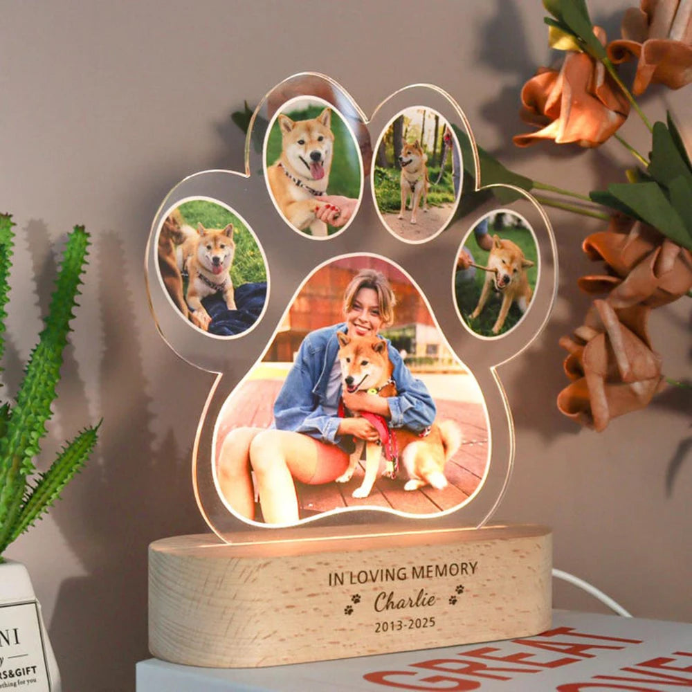 Paw-shaped LED lamp with photos of a person and a dog, placed on a surface with plants and flowers.