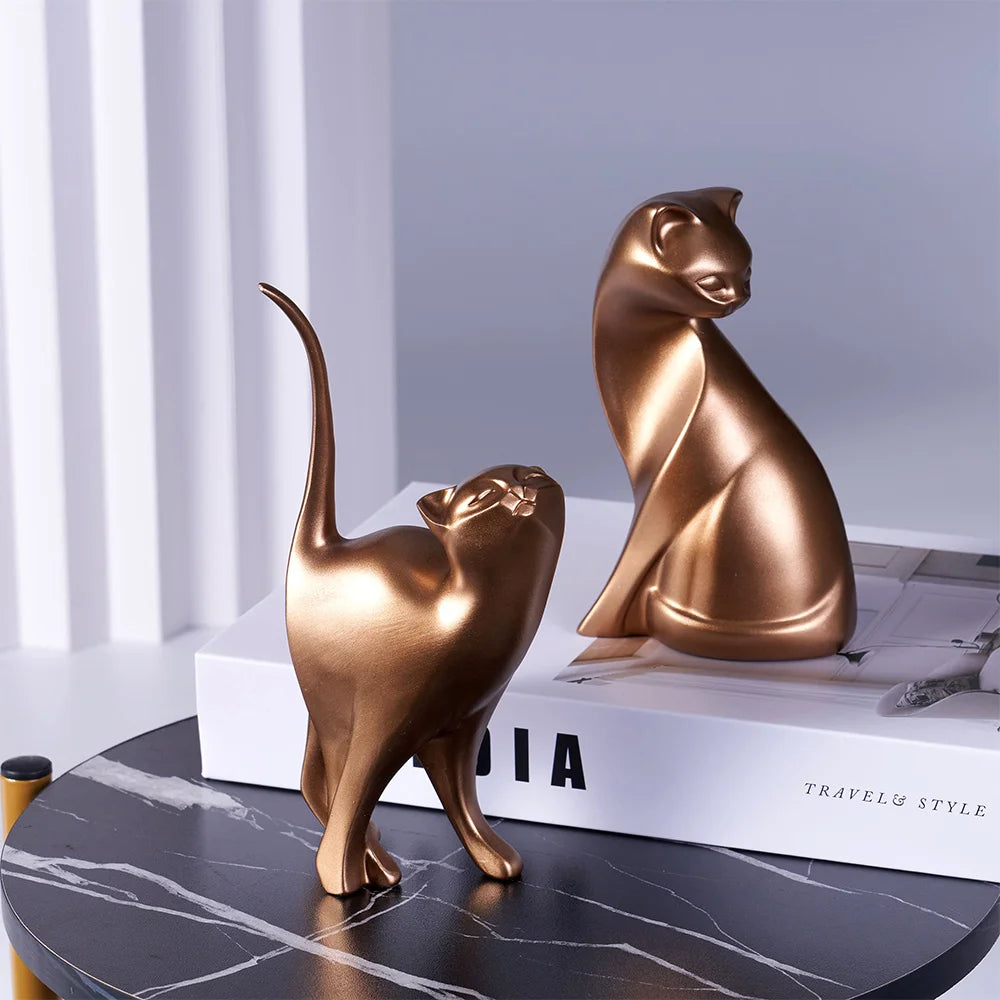 Two bronze cat sculptures on a marble surface with a book in the background.