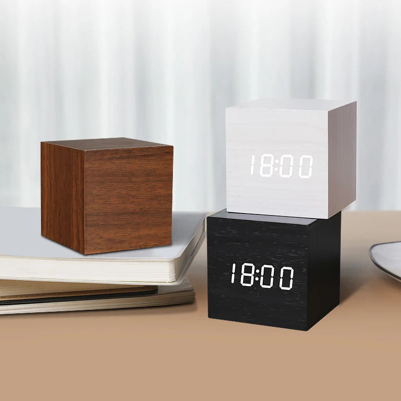 Three cube-shaped digital clocks in different colors on a surface with a light background