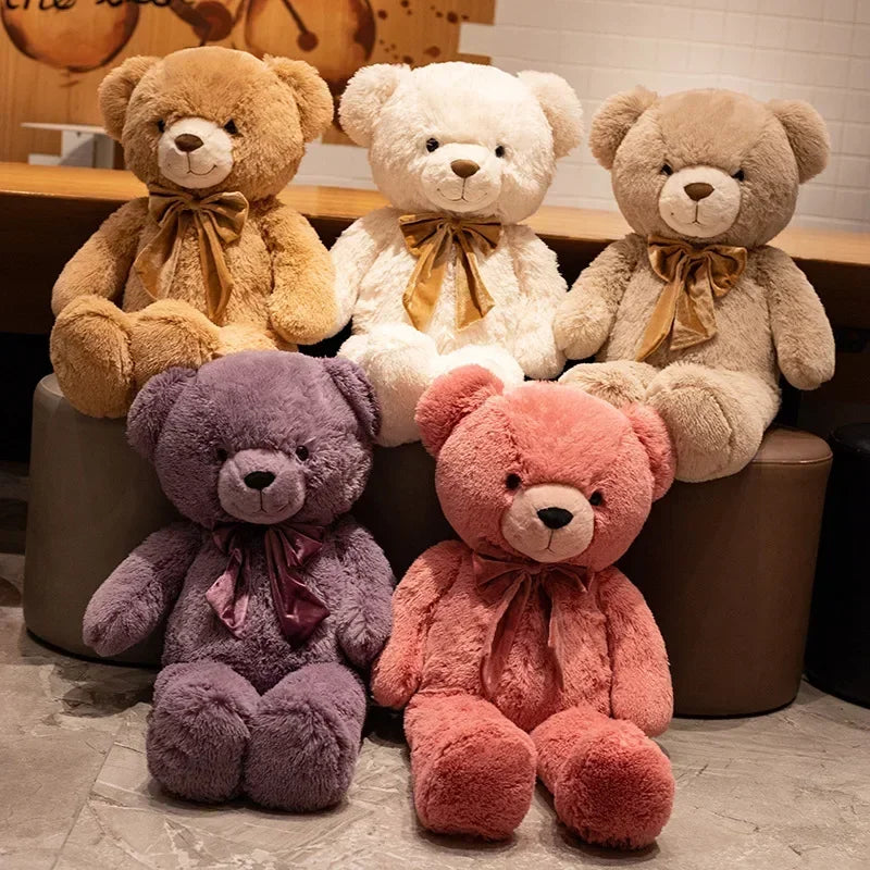 Five teddy bears in different colors with ribbons sitting on a wooden surface.