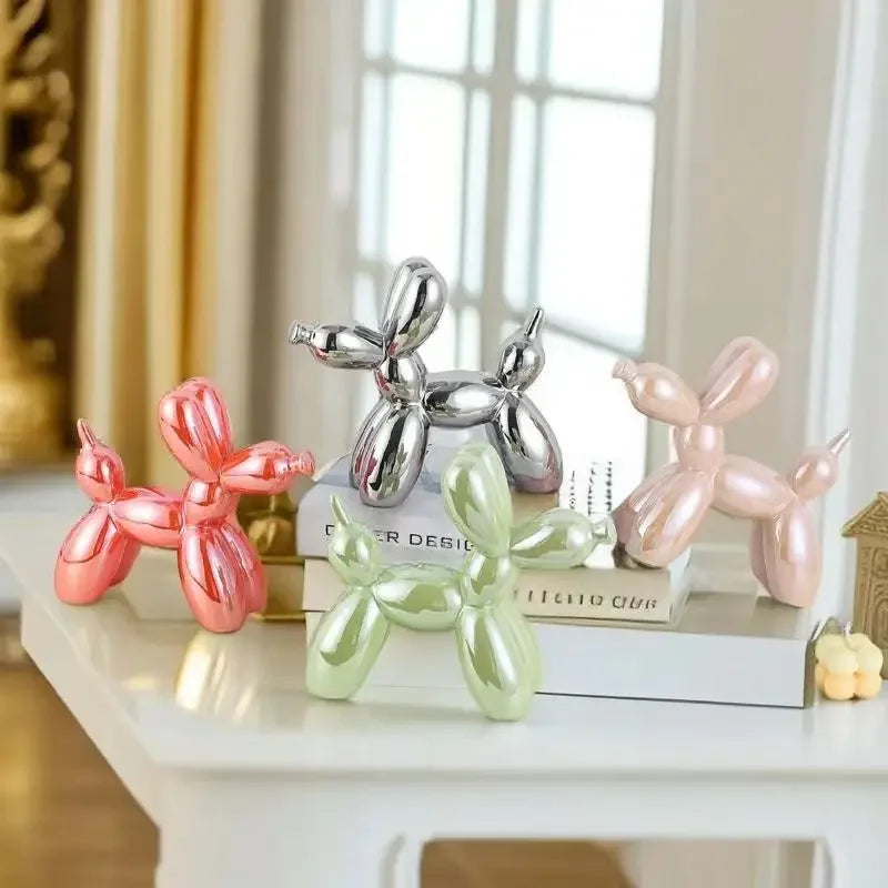 Four balloon dog figurines in pink, green, and silver on a shelf.