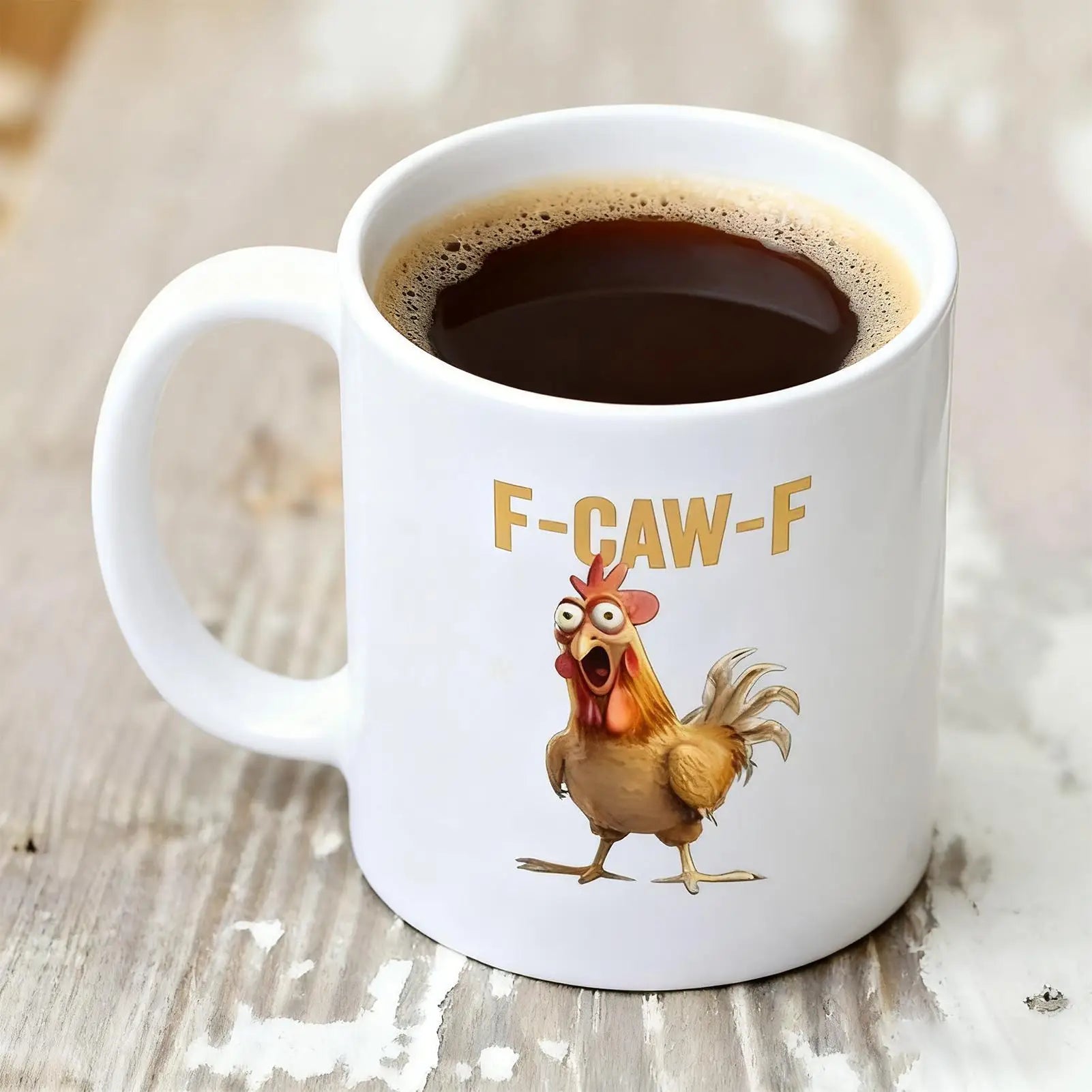 White mug with a cartoon rooster and 'F-CAW-F' text on a wooden surface with coffee.