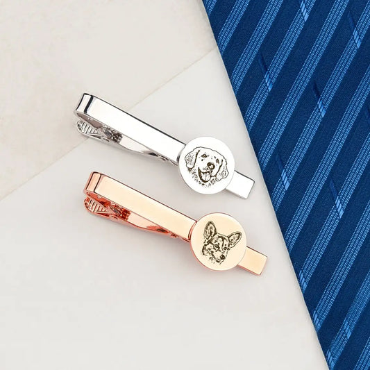 Two tie clips with dog designs on a blue striped tie and white surface