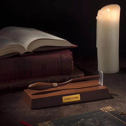 Wooden broom with Nimbus 2000 label on a dark surface with books and a candle.