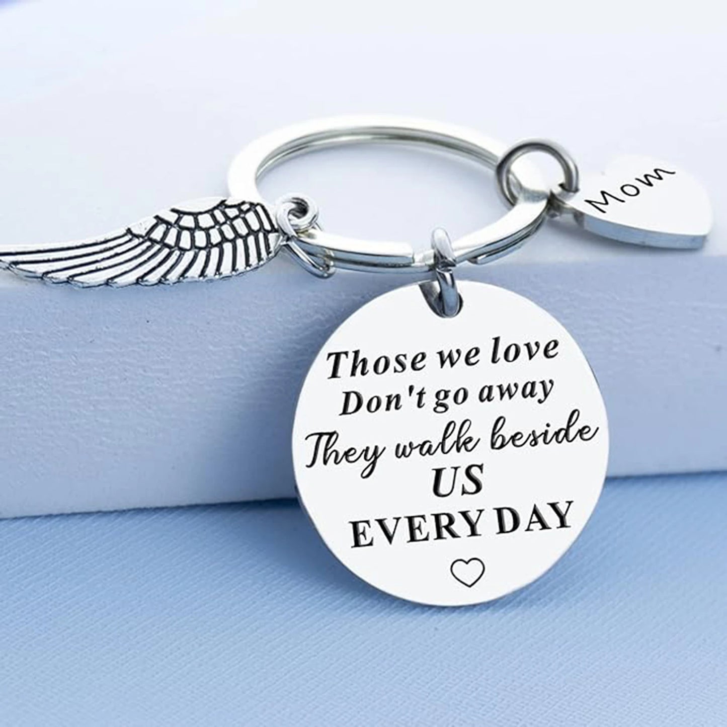 Keychain with angel wing, heart-shaped tag, and engraved message on a light blue background