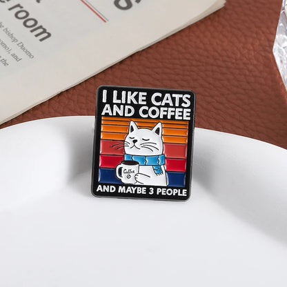 Enamel pin with a cat holding a coffee cup and text 'I like cats and coffee and maybe 3 people' on a white surface.