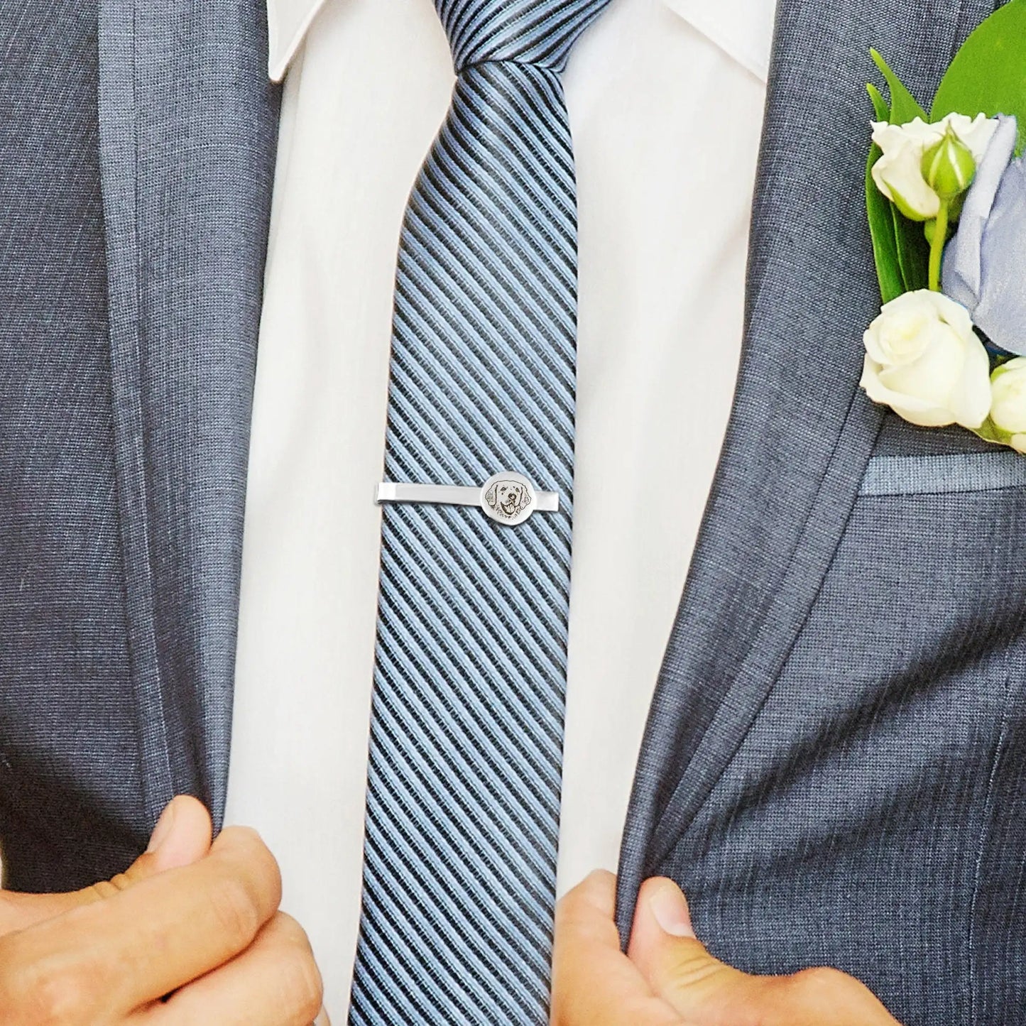 Close-up of a person wearing a gray suit with a white shirt, blue striped tie, and a boutonniere.