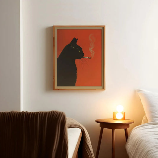 Framed artwork of a black cat smoking a cigarette on an orange background, above a bed with a side table and candle.