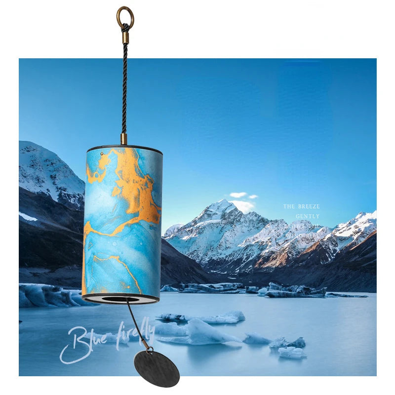 Cylindrical light fixture with blue and gold design against a mountain and lake background