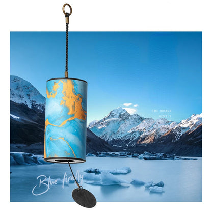 Cylindrical light fixture with blue and gold design against a mountain and lake background