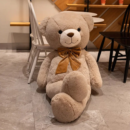 Large teddy bear with a brown bow tie on a stone floor.
