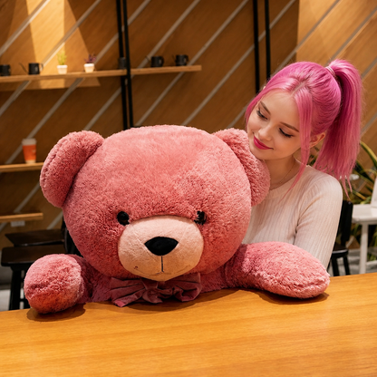 Person with pink hair holding a large pink teddy bear in a casual setting.