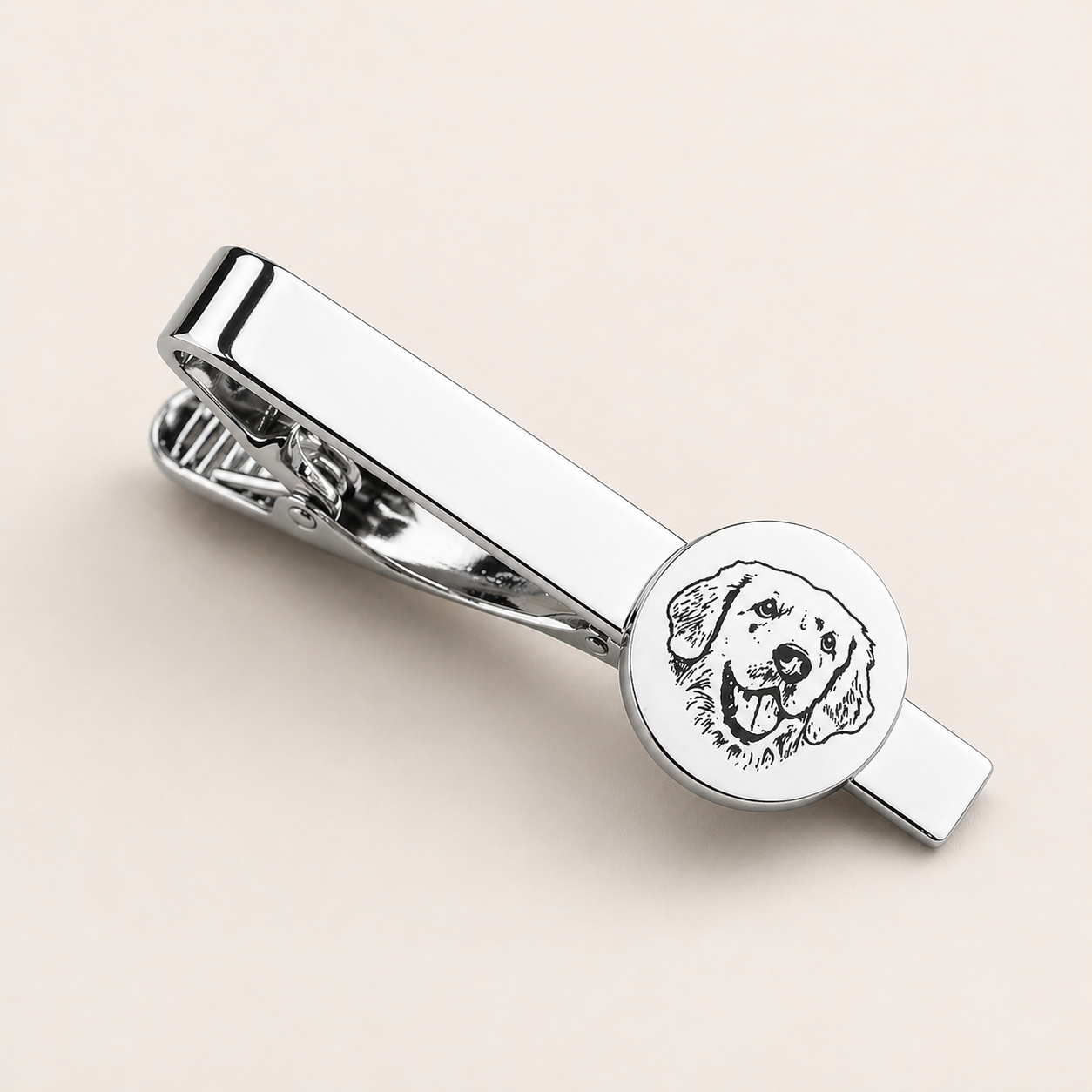 Silver tie clip with engraved dog design on a beige background
